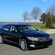 A parked luxury sedan, with a strait of water in the background